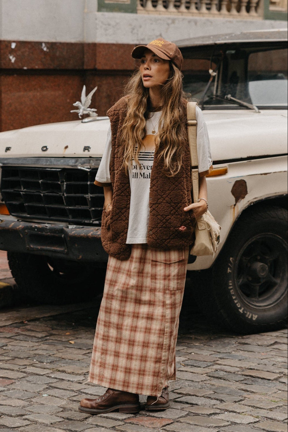 Woman standing in front of a vintage Ford truck wearing a plaid skirt and brown jacket.